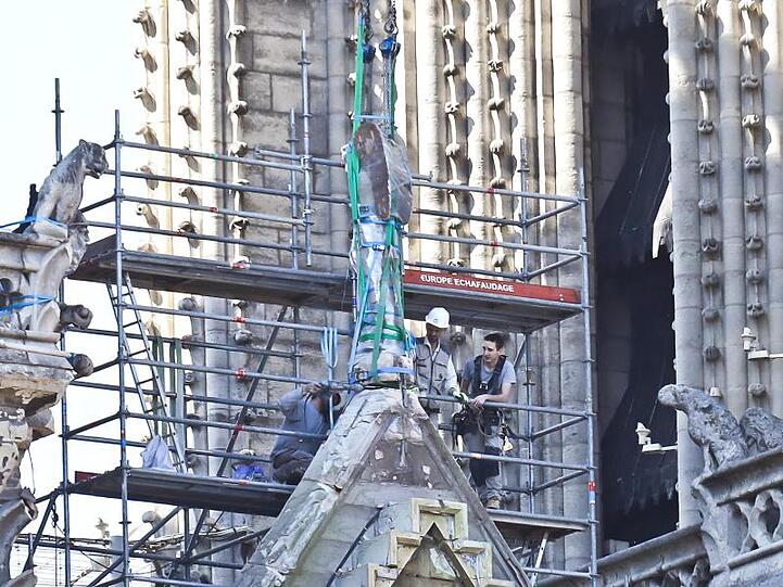Arbeiter bereiten eine Statue auf einem Dach von Notre-Dame auf die Demontage durch einen Kran vor.