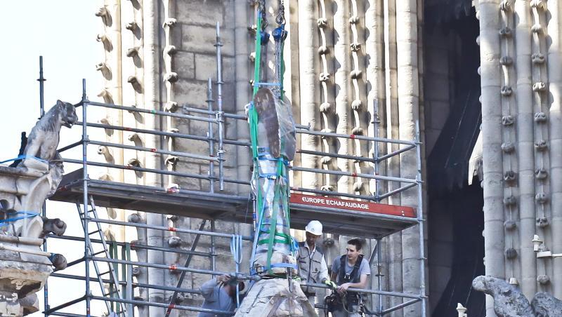 Arbeiter bereiten eine Statue auf einem Dach von Notre-Dame auf die Demontage durch einen Kran vor. Arbeiter bereiten eine Statue auf einem Dach von Notre-Dame auf die Demontage durch einen Kran vor.
