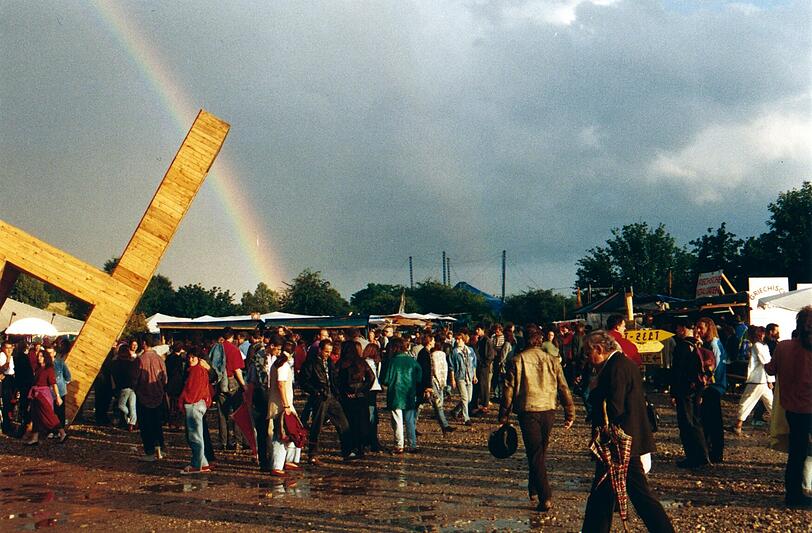 Eine überdimensionale Stuhlinstallation und die Sonne nach dem Regenguss, der einen Regenbogen hinterlassen hat &mdash; eine Tollwood-Szene aus dem Jahr 1994.
