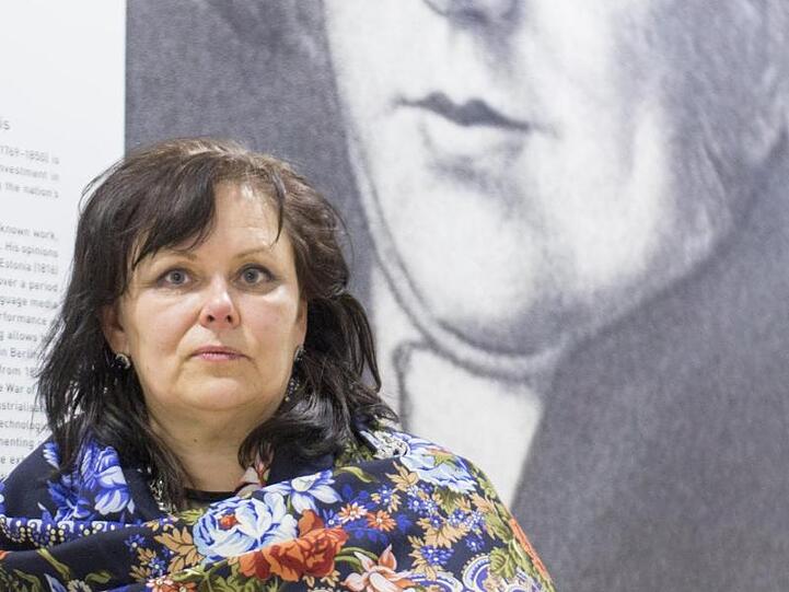 Kuratorin Aija Taimina steht in der Nationalbibliothek am Eingang zur Ausstellung vor einem Poster mit einem Porträt des Publizisten Garlieb Merkel (1769-1850).