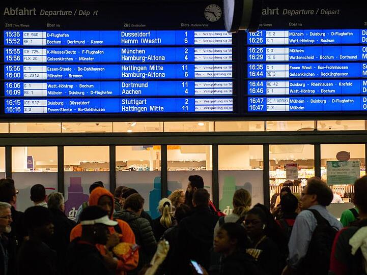 Menschen warten im Essener Hauptbahnhof vor der Anzeigetafel, auf der zahlreiche Zugverspätungen angegeben werden.