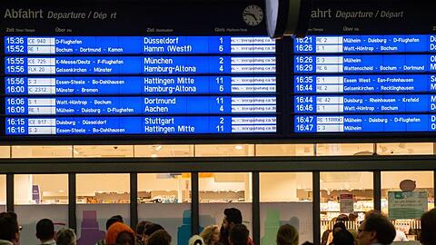 Menschen warten im Essener Hauptbahnhof vor der Anzeigetafel, auf der zahlreiche Zugverspätungen angegeben werden.
