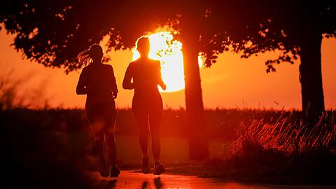 Zwei Frauen joggen am Morgen, während hinter ihnen die Sonne aufgeht.