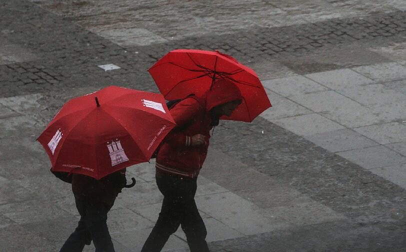 Passanten laufen am 30.03.2015 in Hamburg durch einen Regenschauer über den Rathausmarkt.
