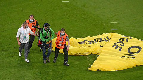 Ein Greepeace-Aktivist, der mit Gleitschirm ins Stadion geflogen ist, wird von der Security abgeführt. Seine Propeller die er auf dem Rücken geschnallt hat sind zersplittert vom Aufprall an der TV-Tribüne, wo er zwei Menschen verletzt hat. (Archiv)