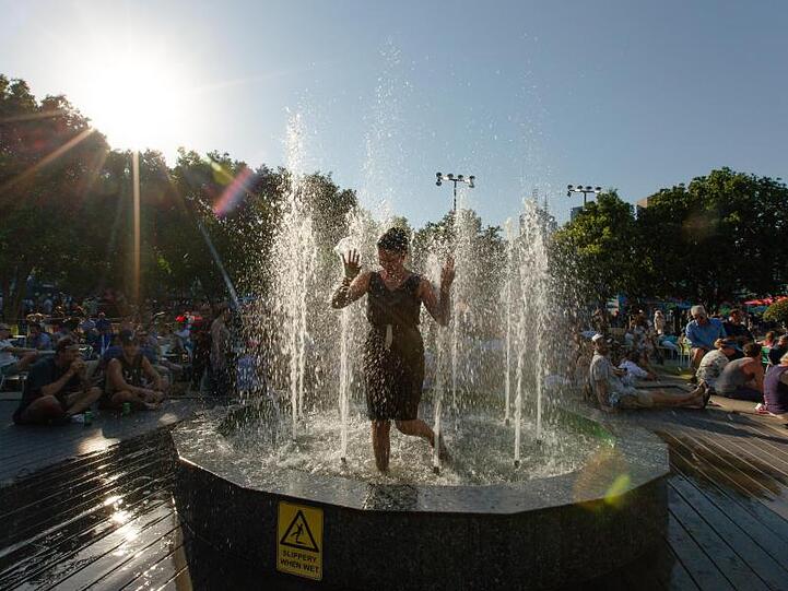 Eine Frau erfrischt sich in kompletter Kleidung in einem Brunnen im Melbourne Park ab.