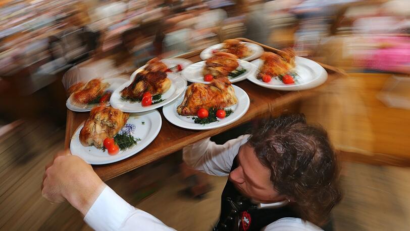 Ein Kellner trägt auf dem Oktoberfest Hendl (Hähnchen) auf einem Tablett.