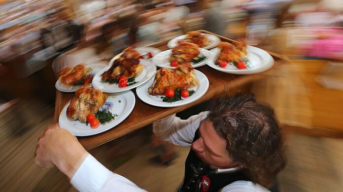 Ein Kellner trägt auf dem Oktoberfest Hendl (Hähnchen) auf einem Tablett.