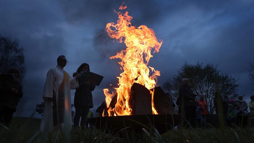 Katholische und evangelische Geistliche stehen während einer ökumenischen Osterfeier im Stadtteil Boxdorf um ein loderndes Osterfeuer.