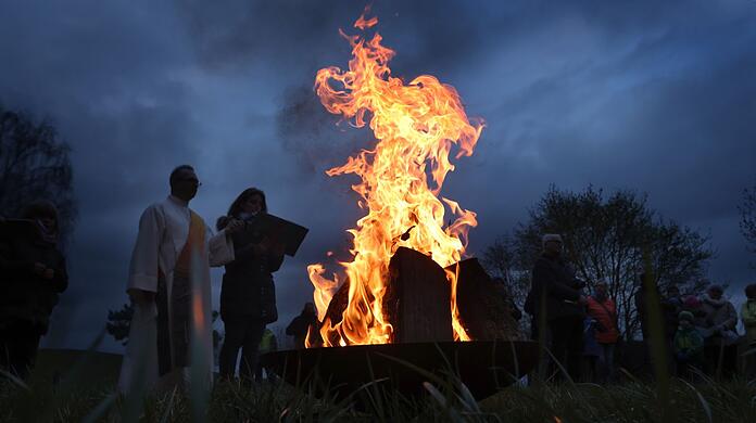 Katholische und evangelische Geistliche stehen während einer ökumenischen Osterfeier im Stadtteil Boxdorf um ein loderndes Osterfeuer.