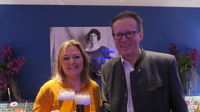 Ein Prost auf die Stiftungs-Gründerin Edith Haberland, die auf dem Bild im Hintergrund zu sehen ist. Vorne stoßen Wiesn-Stadträtin Anja Berger (Grüne) und Augustiner-Chef Martin Leibhard mit einem frisch gezapften Augustiner an.