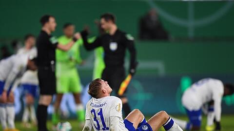 Schalkes Timo Becker sitzt nach dem verlorenen Spiel auf dem Rasen. Ganz hinten (im hellen grün) feiern die Wolfsburger.
