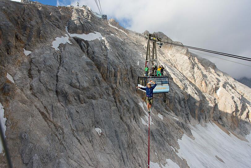Atemberaubende Bilder. Alexander Schulz (23) aus Rosenheim ist in schwindelerregender Höhe über eine Slackline zwischen zwei Zugspitz-Gondeln hin und her balanciert.