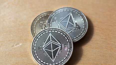Drei physische Nachbildungen von Ethereum-M&uuml;nzen liegen auf einem Holztisch. Die M&uuml;nzen symbolisieren die Kryptow&auml;hrung Ethereum (ETH).