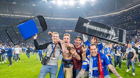 Schalker Fans haben den Rasen gestürmt und bejubeln den Aufstieg.