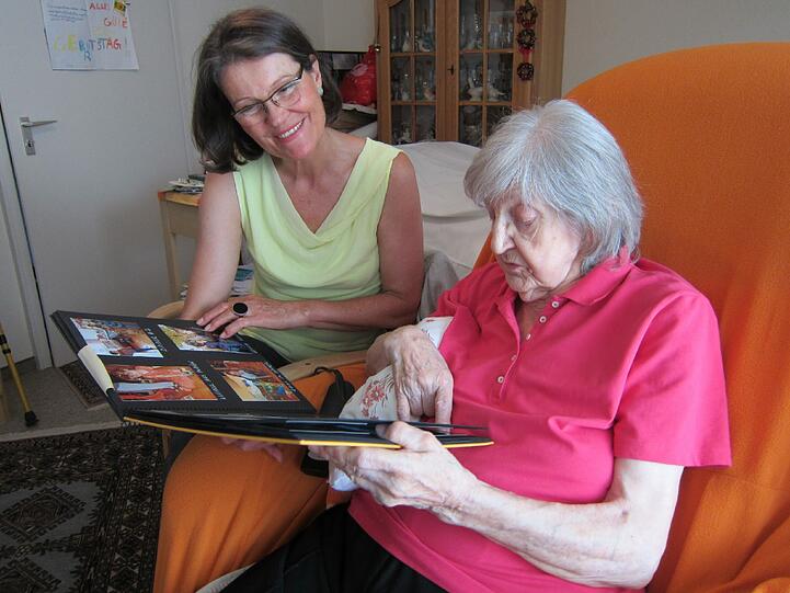 Seniorenbegleiterin Ulrike W. und die 85-jährige Ilse H. schauen sich gemeinsam Familienbilder in einem Fotoalbum an.