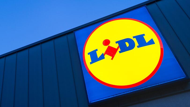 Das Logo eines Lidl-Supermarktes in Berlin-Reinickendorf leuchtet vor dem Abendhimmel.