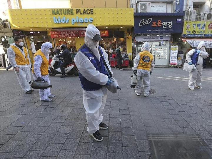 Arbeiter in Schutzkleidung versprühen auf einem Markt in Seoul Desinfektionsmittel.