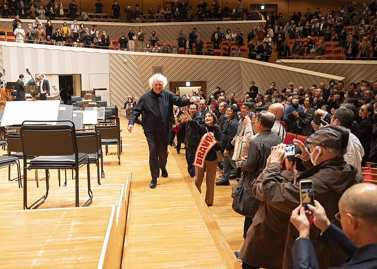 Simon Rattle mit Fans nach dem Konzert in Kawasaki. Während der der Corona-Pandemie waren laute Rufe in japanischen Konzertsälen verboten, daher brachten manche Besucher Transparente mit und behielten dies bis heute bei. Ohnehin gilt in Japan lautes Geschrei als unhöflich.