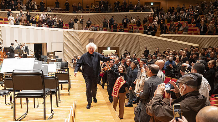 Simon Rattle mit Fans nach dem Konzert in Kawasaki. Während der der Corona-Pandemie waren laute Rufe in japanischen Konzertsälen verboten, daher brachten manche Besucher Transparente mit und behielten dies bis heute bei. Ohnehin gilt in Japan lautes Geschrei als unhöflich.