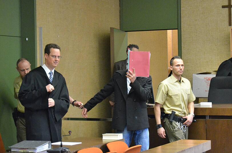 Ali S.(22) hält sich einen roten Aktenordner vor sein Gesicht. Links neben ihm sein Verteidiger Markus Meißner.