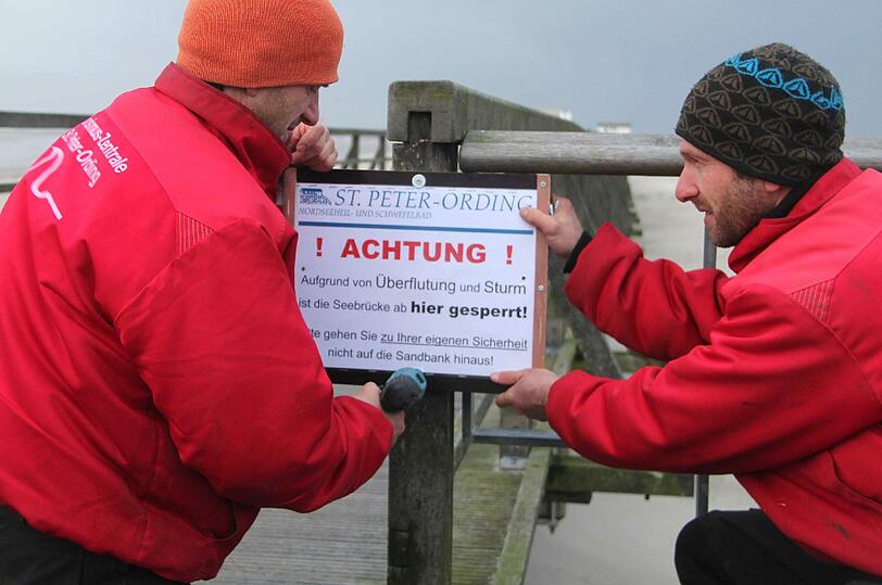 Rüsten für den Sturm: Mitarbeiter der Tourismuszentrale befestigenein Warnschild an der Seebrücke in St. Peter-Ording.