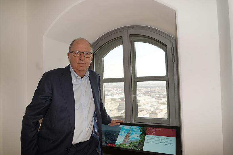 Dompfarrer Klaus Peter Franzl vor einem der 16 Domfenster mit Touchscreen. Draußen sind Oper und Residenz zu sehen.