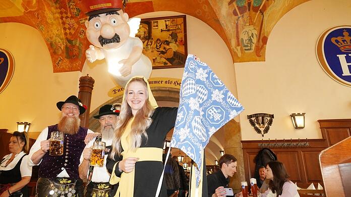 Das Münchner Kindl Viktoria Ostler hält die blaue Maske von Aloisius in der Hand. Die Gäste Thorsten Schwerdt (l.) und Harald Gieß prosten zu.