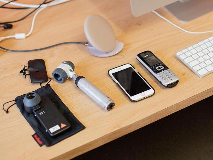 Ein Computer, ein Handy, ein Telefon sowie Untersuchungsgeräte für Dermatologie liegen in der Praxis einer Fachärztin.