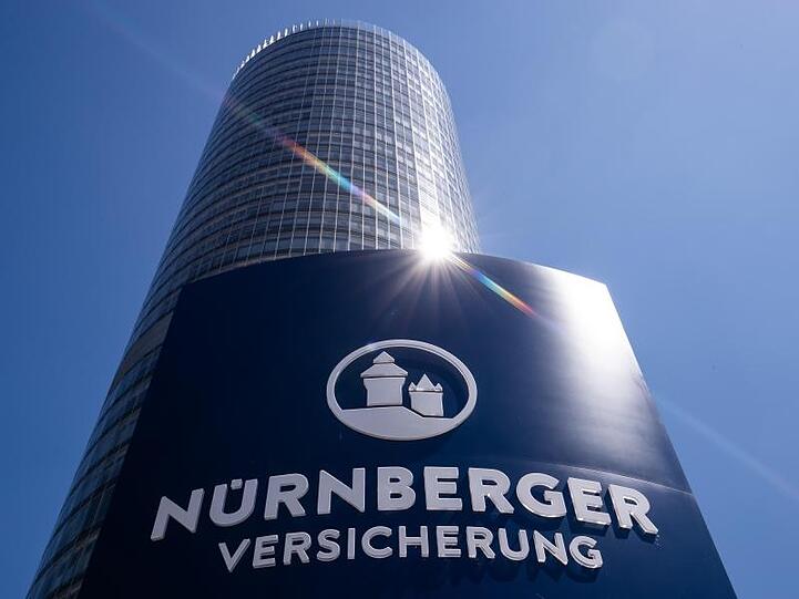 Der Schriftzug der Nürnberger Versicherungsgruppe mit dem Logo des Unternehmens stehen auf einer Säule vor dem Firmensitz, dem 135 Meter hohen Business Tower. Foto: Daniel Karmann/dpa/Archivbild