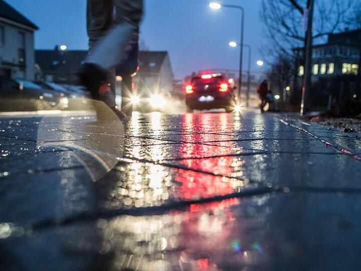 Auf einem Gehweg spiegelt sich der Lichtschein von Autos und Straßenlaternen. Foto: Frank Rumpenhorst/Archiv