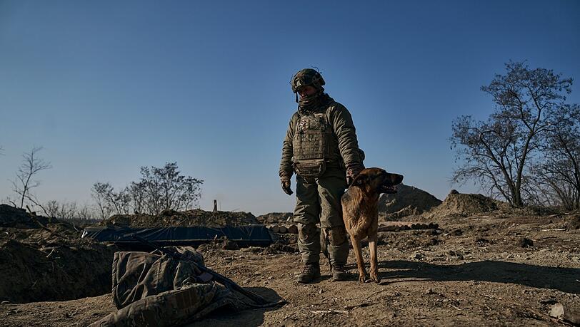 Ein ukrainischer Soldat steht mit seinem Hund an einem Graben in Bachmut.
