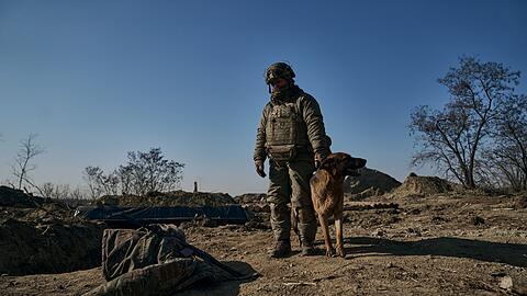 Ein ukrainischer Soldat steht mit seinem Hund an einem Graben in Bachmut.