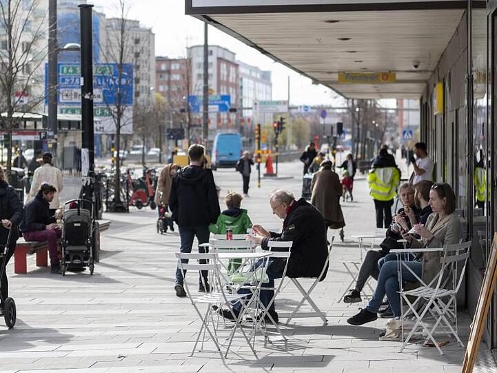 Menschen sitzen im Stadtzentrum von Stockholm vor einem Eiscafe.