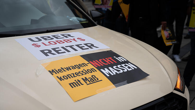 Zwei Schilder mit der Aufschrift "Uber $ Lobby $ Reiter" und "Mietwagenkonzession mit Maß – Nicht in Massen" kleben bei der Demo auf einem Taxi. Zwei Schilder mit der Aufschrift "Uber $ Lobby $ Reiter" und "Mietwagenkonzession mit Maß – Nicht in Massen" kleben bei der Demo auf einem Taxi.