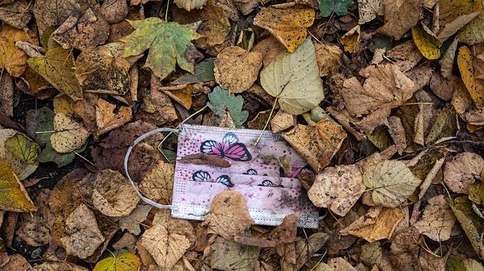 Ein rosafarbener Mund-Nasen-Schutz gegen das Virus im Herbstlaub.