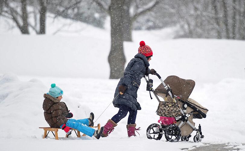 Spaß für den kleinen Rodler, Sport für die Mama: Eine Frau schieb den Kinderwagen in München durch den Schnee und zieht ihr zweites Kind auf dem Schlitten hinter sich her.