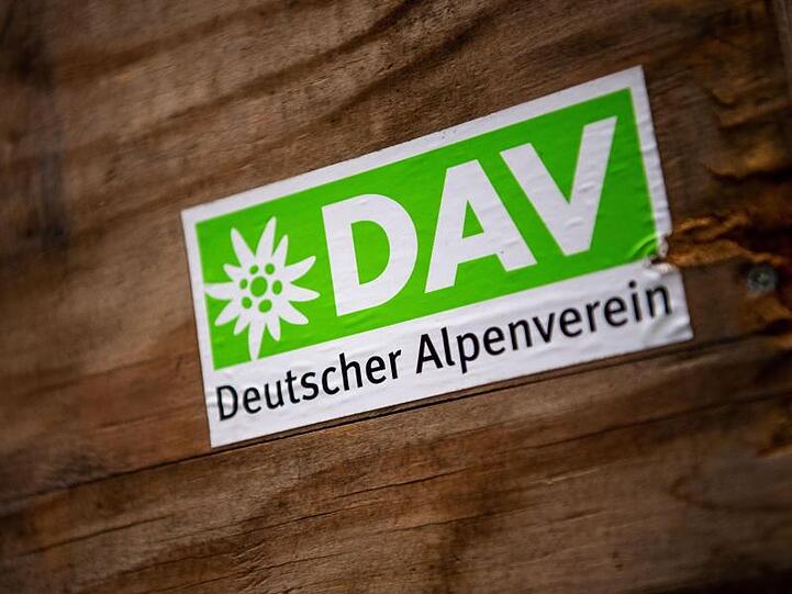 Das Logo des Deutschen Alpenverein (DAV) klebt auf einer Holzbox. Foto: Lino Mirgeler/dpa