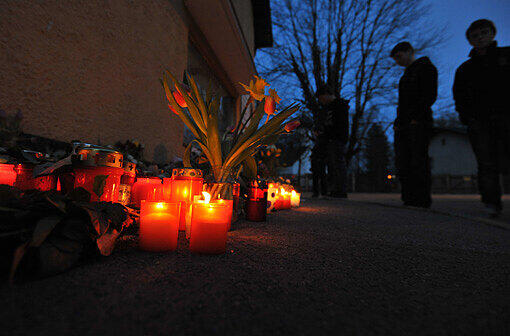 Vor einem Meer aus Blumen, Kerzen und Teddybären stehen Menschen vor dem Haus, in dem die Kinder gelebt haben.
