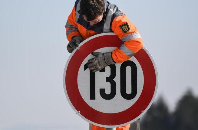 Ein Straßenwärter montiert an einer Autobahn ein Schild zur Geschwindigkeitsbegrenzung.