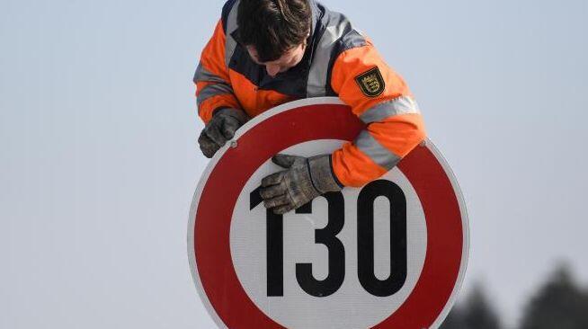 Ein Straßenwärter montiert an einer Autobahn ein Schild zur Geschwindigkeitsbegrenzung.