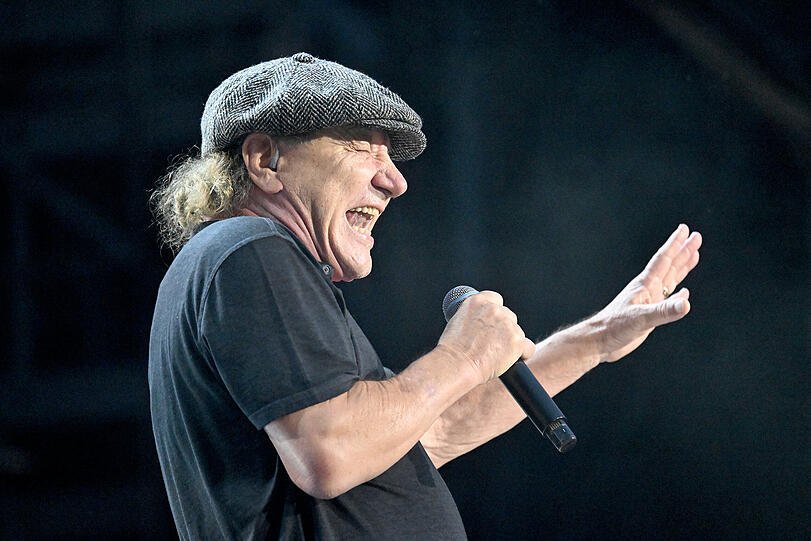 Brian Johnson strahlt mit Schiebermütze und schlichtem Polohemd  Kumpelhaftigkeit pur aus.