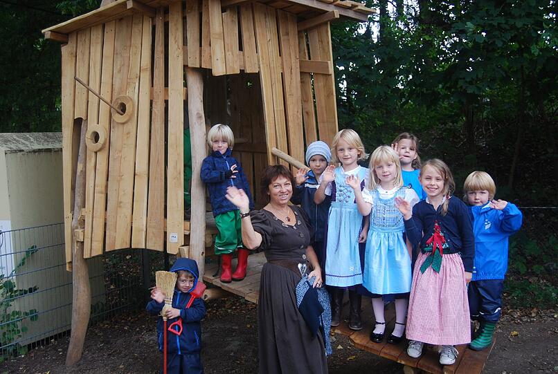 Strahlende Kinder und die zufriedene Kindergartenleiterin Dagmar Wagner freuen sich über das von der Bürgervereinigung Obermenzing e.V. gestiftete Stelzenhaus, das den Abschluss der Gartensanierung des Pfarrkindergartens markiert.