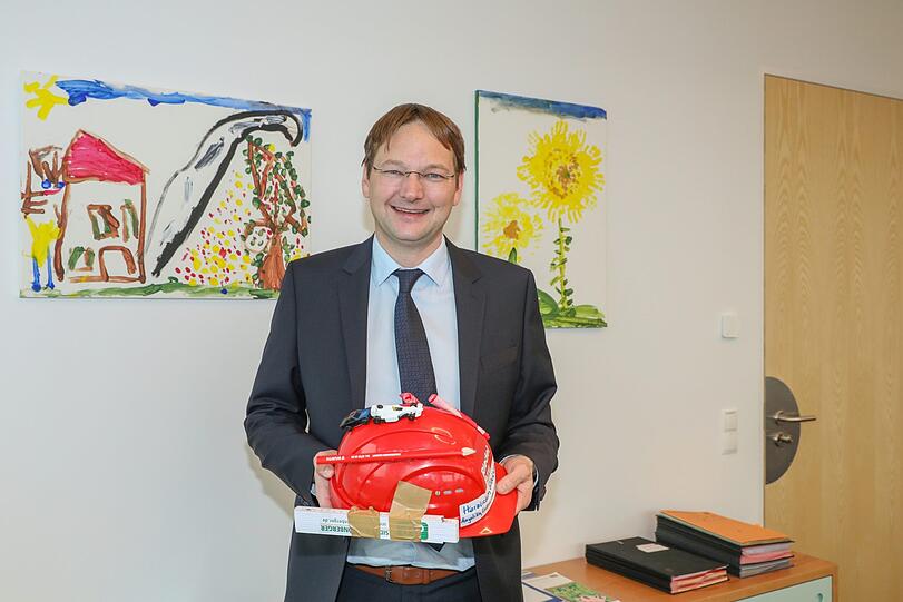 Bau- und Verkehrsminister Hans Reichhart in seinem Büro. Den Bauhelm hat er von seinem Onkel, die Bilder haben seine Kinder gemalt.