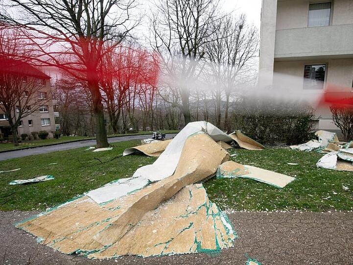 Der Putz eines Mehrfamilienhauses liegt vor dem Eingang, während ein Absperrband der Feuerwehr im Wind flattert.