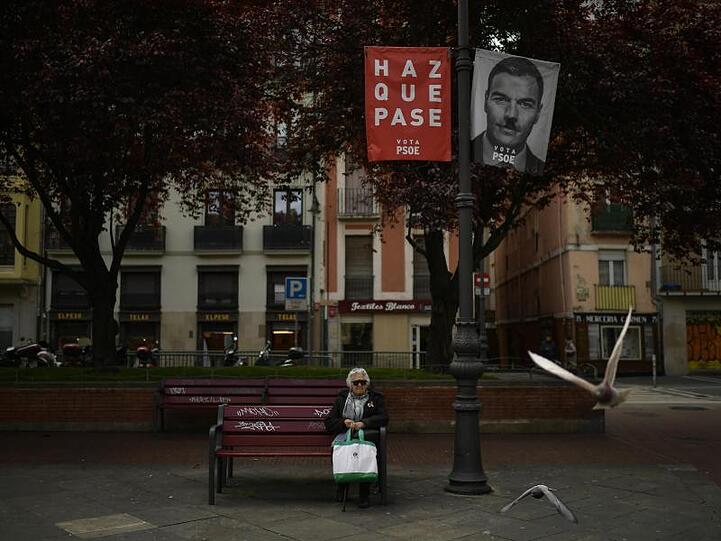 Eine Frau sitz auf einer Bank neben einem Wahlbanner für Sanchez, der spanische Ministerpräsident, mit dem Satz, "Mach es möglich". Sanchez liegt zwar in Umfragen seit Wochen mit rund 30 Prozent vorne.