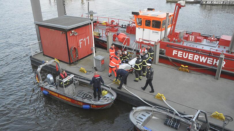 Eine Leiche wird von einem Boot der Feuerwehr Hamburg auf einen Steg im Hafen getragen.