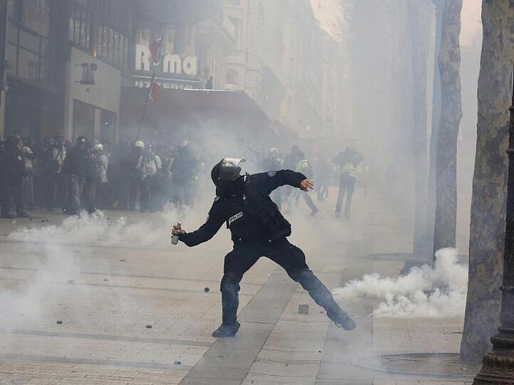 Ein Polizist wirft Tränengas in Richtung der demonstrierenden "Gelbwesten" auf den Champs-Elysees.