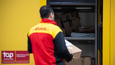 Ein Post-Mitarbeiter trägt ein Paket in einen Lieferwagen.