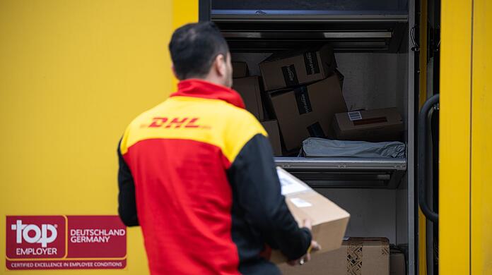 Ein Post-Mitarbeiter trägt ein Paket in einen Lieferwagen.